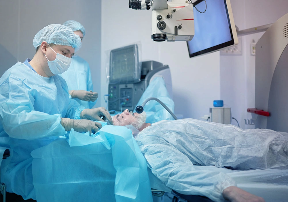 A masked surgeon treating a patient's eye under a surgical machine in a hospital operating room.