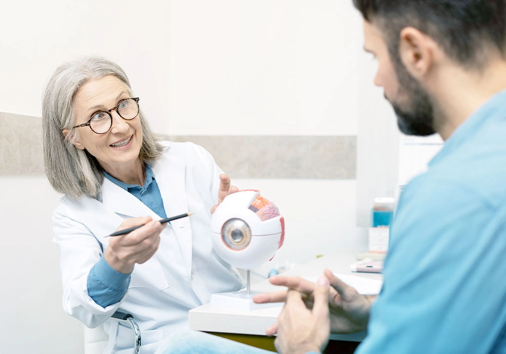 Doctor pointing at a human eye model while talking to a patient.