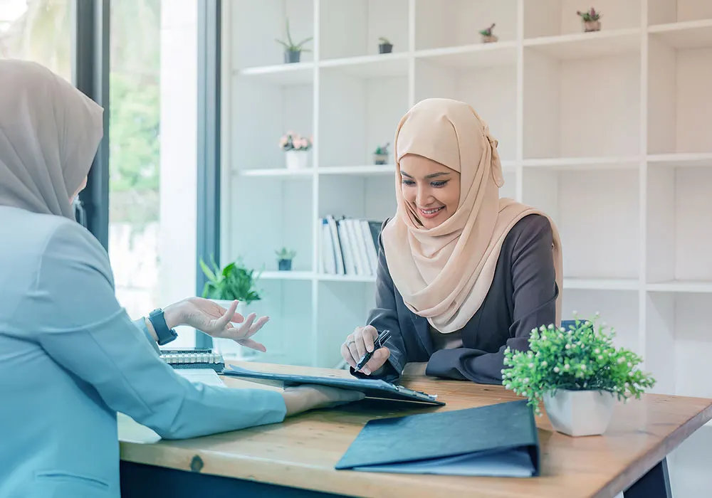 Two women wearing hijabs discussing LASIK eye surgery cost in the UAE at a medical office, one smiling while reviewing documents with a consultant.